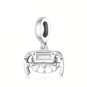 May include: A silver charm pendant shaped like a steering wheel, with a central display and various button details. The charm has a loop at the top for attaching to a bracelet or necklace. The design is highly detailed and reflects light.