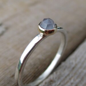 May include: A silver ring with a hammered finish and a grey gemstone set in a gold bezel.