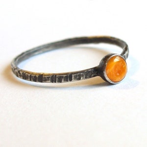 May include: A silver ring with a textured band and a small orange gemstone.