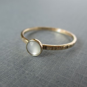 Könnte beinhalten: Ein schlichter Goldring mit einem weißen Opal-Edelstein. Die Ringschiene ist gehämmert für eine strukturierte Optik.