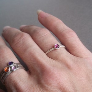 May include: Two silver rings with colourful gemstones. The top ring has a single pink gemstone. The bottom ring has three gemstones: orange, pink, and purple.