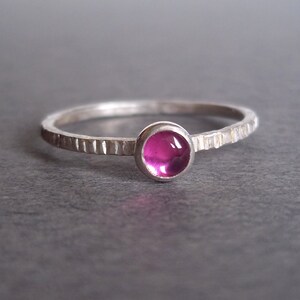 May include: A silver ring with a textured band and a pink gemstone.