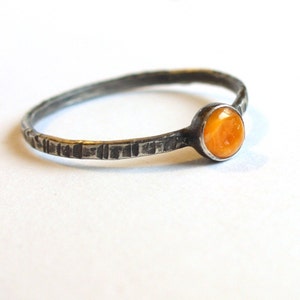 May include: A silver ring with a textured band and a round orange gemstone.
