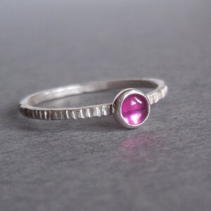 May include: A silver ring with a textured band and a pink gemstone.