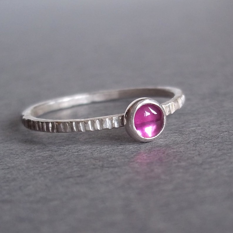 May include: A silver ring with a textured band and a pink gemstone.