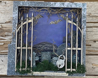 May include: A shadow box diorama depicting a graveyard scene with a metal gate, tombstones, and bats against a blue backdrop. The gate is locked with a silver padlock. The text reads "...ed the chain holding the gate closed."