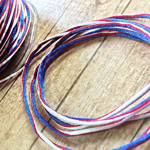 May include: Red, white, and blue striped cord, wound in a circle on a wooden surface.