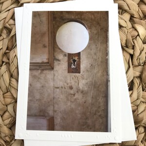 以下が含まれることがあります： 古びた木製のドアに取り付けられた、さび付いた鍵穴のある白い磁器製のドアノブ