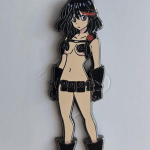 May include: A black and white enamel pin featuring an anime character with black hair, red eyes, and a black and white outfit. The character is wearing a black leather jacket with a red symbol on the chest.