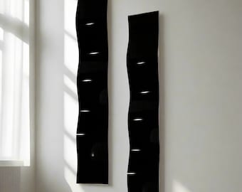 May include: Two tall, black, wavy wall panels with a glossy finish are mounted on a white wall. Each panel has several horizontal white accent lights. The panels are positioned near a window with white curtains.