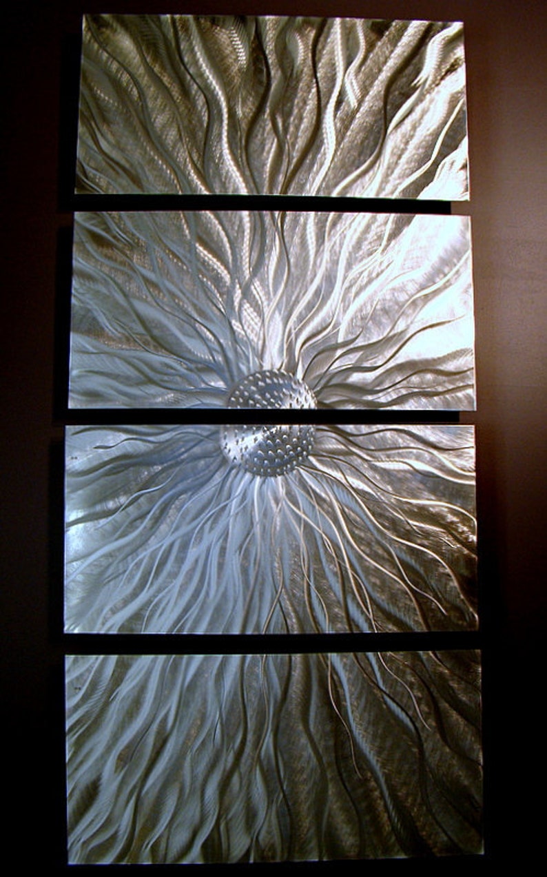 May include: Abstract metal wall art comprising four rectangular panels. Each panel displays a textured, flowing design in silver and grey tones, reminiscent of stylized floral or sunburst patterns. The artwork is mounted on a dark background.
