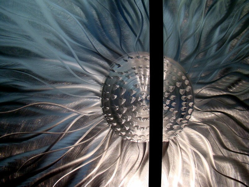 May include: Abstract metal wall art with a central textured sphere and flowing lines radiating outwards. The artwork has a metallic silver and blue colour scheme, creating a modern aesthetic. A vertical black line divides the piece.