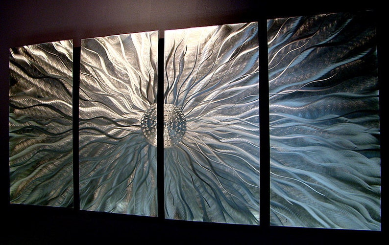 May include: Abstract metal wall art in four panels. The artwork shows a central, textured sphere with radiating lines and a metallic silver and blue colour palette. The panels are mounted on a dark wall.