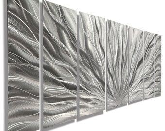 May include: Abstract metal wall art in silver tones. The artwork is made up of several panels, forming a textured design. The panels display flowing, wave-like patterns that extend outwards, giving a sense of movement and depth. The artwork is suitable for any room.