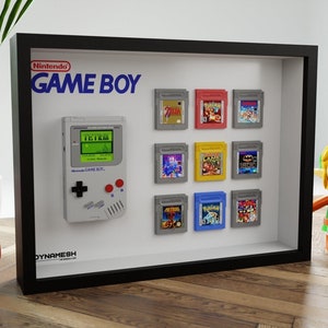 Op de afbeelding: Een ingelijste display met een Nintendo Game Boy en verschillende spelcartridges. De Game Boy is grijs met een groen scherm met Tetris. De lijst bevat het Nintendo Game Boy-logo en staat tegen een witte achtergrond.