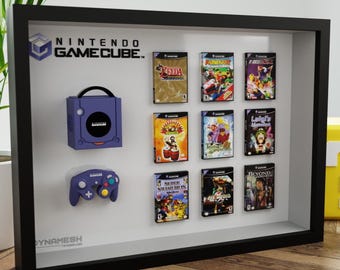 May include: A framed display featuring a Nintendo GameCube console, controller, and game cartridges. The console and controller are purple. The game cases are displayed in a black frame, with the Nintendo GameCube logo at the top. A yellow question mark block is in the background.