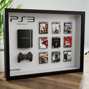 Op de afbeelding: Een zwarte, ingelijste vitrine met een PlayStation 3 console, een controller en negen videospelverpakkingen. De console is zwart en heeft de tekst "PlayStation 3" op de voorkant. De controller is zwart en heeft het Sony-logo. De spelverpakkingen zijn allemaal in verschillende kleuren en hebben verschillende speltitels. De vitrine staat op een houten oppervlak.