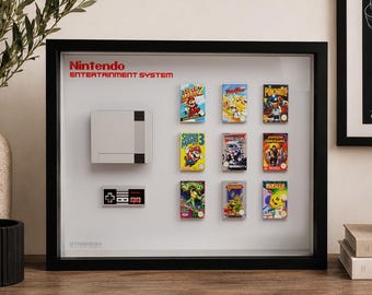 May include: A black-framed shadow box display featuring a miniature Nintendo Entertainment System console, a controller, and nine classic game cartridges arranged in a grid. The white background includes the red Nintendo Entertainment System logo.