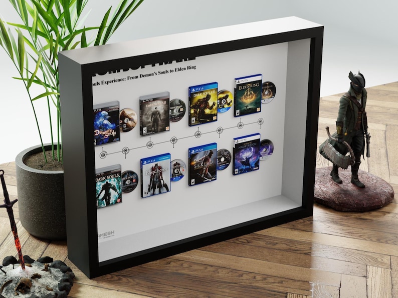 May include: A framed display featuring video game cases and discs from the "Souls" series, including "Demon's Souls" and "Elden Ring." The black frame houses the games, arranged along a timeline. A figurine stands to the right.