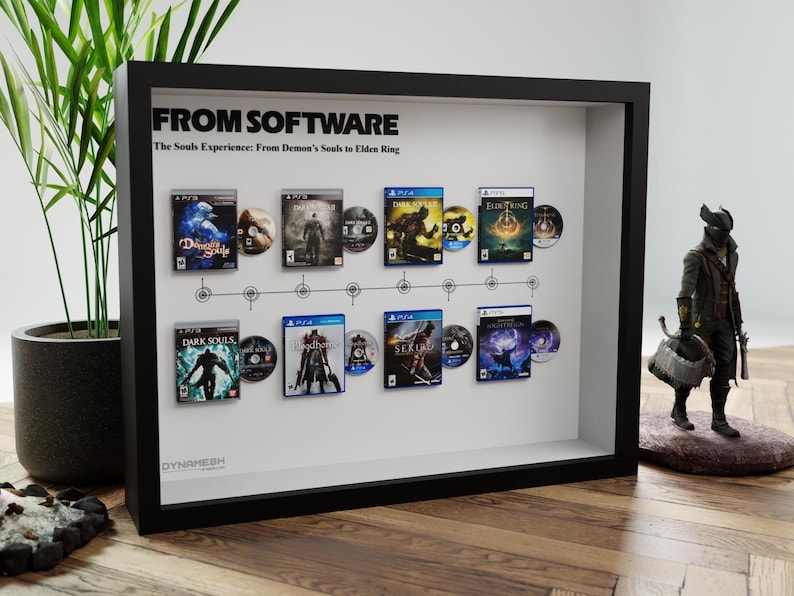 May include: A framed display featuring video game cases and discs from the "Souls" series, including "Demon's Souls" and "Elden Ring." The black frame showcases the games in chronological order, with a small figurine on the right.