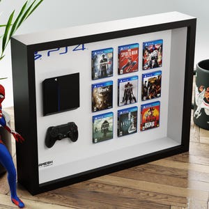 Peut inclure: Un cadre de présentation noir contenant une console de jeu miniature noire, une manette de jeu noire et neuf boîtiers de jeux miniatures disposés en grille.