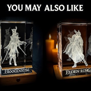 May include: Two illuminated glass cubes with engraved figures, one labeled "Bloodborne" and the other "Elden Ring." The cubes sit on wooden bases, with candles in the background. The text "YOU MAY ALSO LIKE" is at the top.