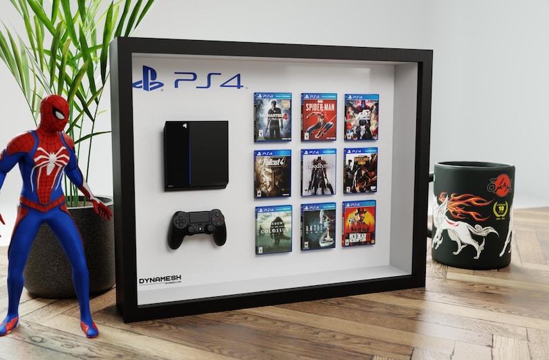 Peut inclure: Un cadre de présentation noir de type boîte vitrine contenant une console, une manette et neuf boîtiers de jeux fixés sur un fond blanc.