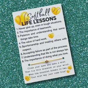 May include: A white card with the words "Softball Life Lessons" and a list of life lessons. The card features softball graphics and a gold bracelet with a star charm. The card is on a glittery green surface.