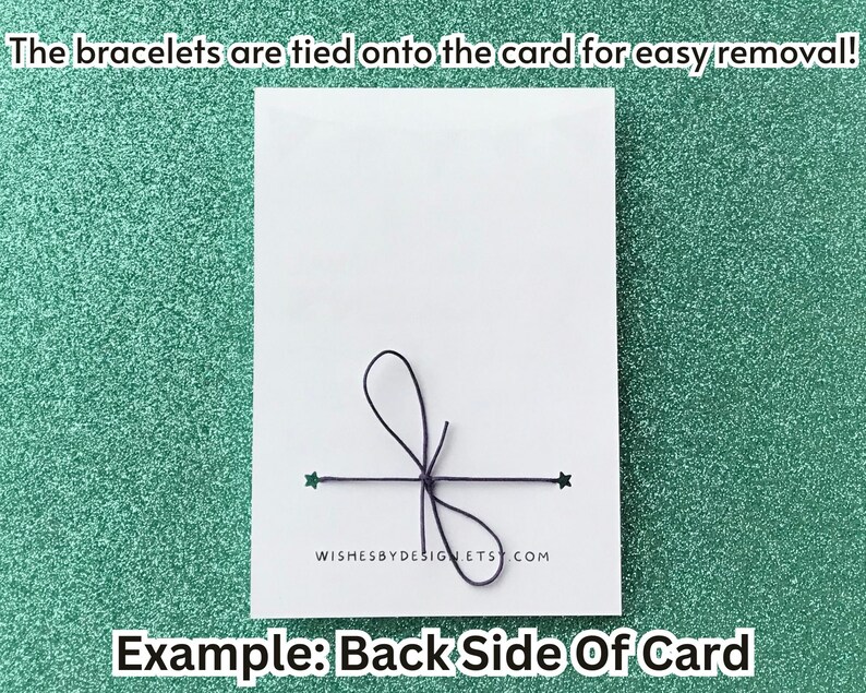 Peut inclure: Une carte blanche avec un n&oelig;ud noir et des d&eacute;tails de ficelle, avec le texte "WISHESBYDESIGNETS.COM". Le texte "Les bracelets sont attach&eacute;s &agrave; la carte pour un retrait facile !" est en haut, et "Exemple : Verso de la carte" est en bas. Le fond est un vert d'eau scintillant.