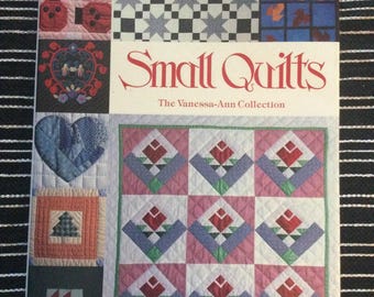 以下が含まれることがあります： 「Small Quilts」というタイトルの本の表紙。様々なキルトブロックのデザインが特徴です。表紙には、花柄、幾何学模様、ハート型など、さまざまなキルトパターンが掲載されています。この本は「The Vanessa-Ann Collection」の一部です。