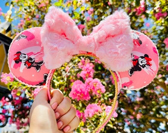 May include: Pink Minnie Mouse ears headband with a large pink bow and a pink and white patterned design featuring Minnie Mouse.