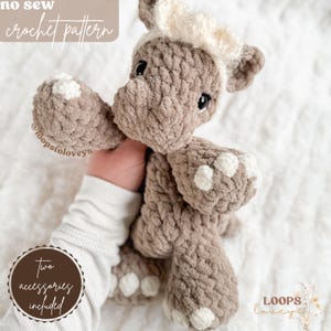 Può includere: Un giocattolo di peluche di rinoceronte all'uncinetto con una fascia bianca. Il rinoceronte è marrone e ha macchie bianche sui piedi. Il giocattolo è tenuto da una mano. Il testo "no sew crochet pattern" è nella parte superiore dell'immagine. Il testo "two accessories included" è in un cerchio nella parte inferiore sinistra dell'immagine. Il testo "LOOPS loveys" è nella parte inferiore destra dell'immagine.