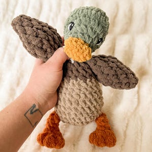 May include: A plush toy duck with brown, tan, and green fabric. The duck has a yellow beak and black eyes.