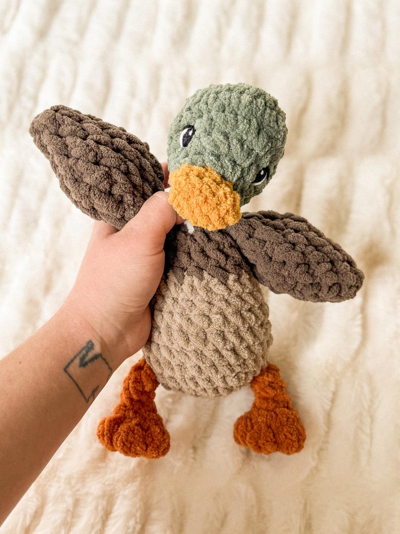 May include: A plush toy duck with brown, tan, and green fabric. The duck has a yellow beak and black eyes.