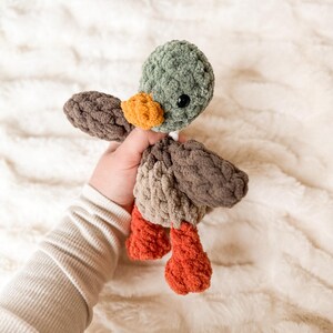 May include: A crocheted plush duck toy with brown, green, and orange colors. The duck has a small beak and large eyes.