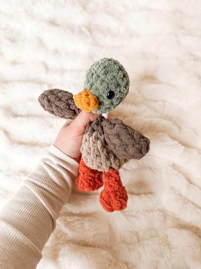 May include: A crocheted plush duck toy with brown, green, and orange colors. The duck has a small beak and large eyes.