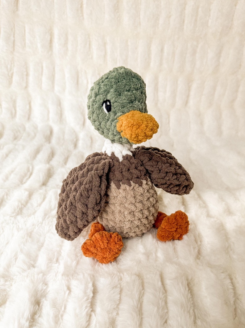 May include: A crocheted plush duck toy with brown, green, and orange yarn. The duck has a small, white beak and black eyes.