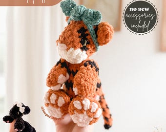 May include: Crochet pattern for a tiger amigurumi toy with a teal bow. The toy is orange and black with white paw pads. The pattern includes no-sew accessories. The text "no sew accessories included" is on a white circle with a black border.