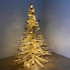 May include: A wooden Christmas tree with a unique design. The tree is constructed from light-coloured wooden slats, arranged to create a tree shape. It is adorned with small, warm white lights and decorative gold bows. The tree stands approximately 152 cm tall.