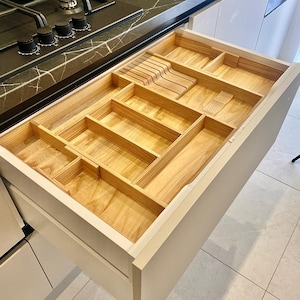 May include: A white drawer with a wooden cutlery organizer insert. The organizer has multiple compartments for different sized utensils.