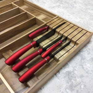 May include: A set of six black-bladed knives with red handles, presented in a wooden organiser. The knives have a sleek, modern design, with a silver accent at the base of the handle. The wooden organiser has multiple compartments.