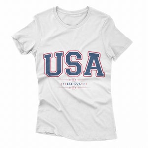 May include: White t-shirt with a blue and red graphic that says "USA EST. 1776" in a vintage collegiate style.