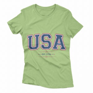 May include: A light green t-shirt with a navy blue and red graphic that says "USA EST. 1776" with stars.