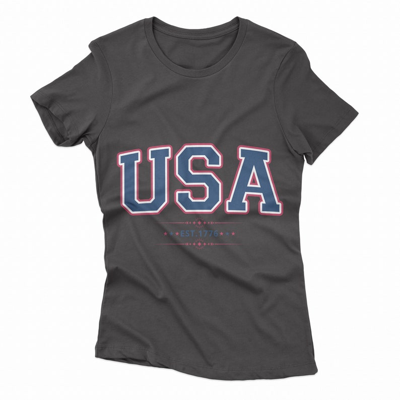May include: A charcoal grey t-shirt with a navy blue and red "USA" graphic and the text "EST. 1776" in red.