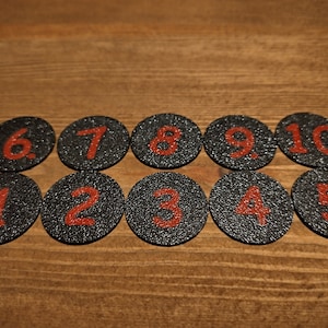 May include: Ten black round discs with red numbers 1 through 10 on them.