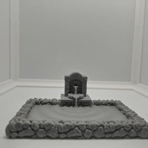 May include: A grey stone fountain with a small pool of water. The fountain is made of a textured material and has a simple design.