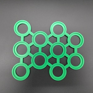 Op de afbeelding: Een groene, zeshoekige kunststof mal met 12 ronde uitsparingen. De mal is ontworpen om kleine ronde voorwerpen te bevatten.