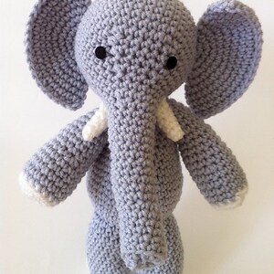 May include: A gray crocheted elephant stuffed animal with white crocheted accents on the ears, trunk, and feet. The elephant has black button eyes.