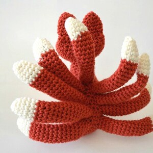 May include: A crocheted octopus made with red and white yarn. The octopus has eight tentacles with white tips.