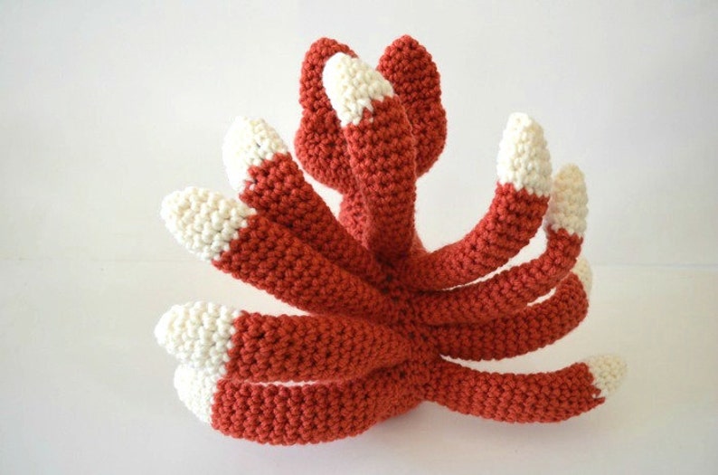May include: A crocheted octopus made with red and white yarn. The octopus has eight tentacles with white tips.